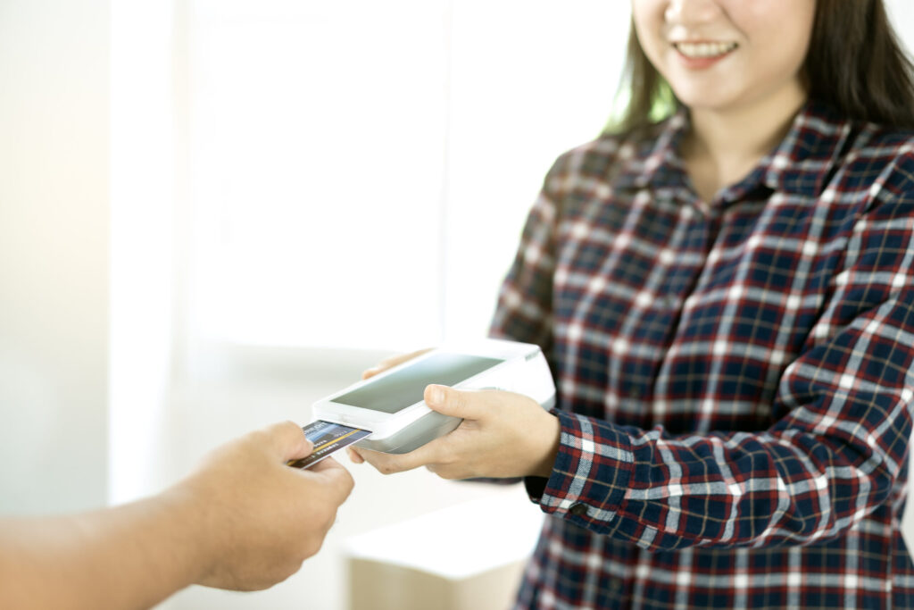 Close-up of asian entrepreneur using EDC to receive credit card for payment from customer in her store.